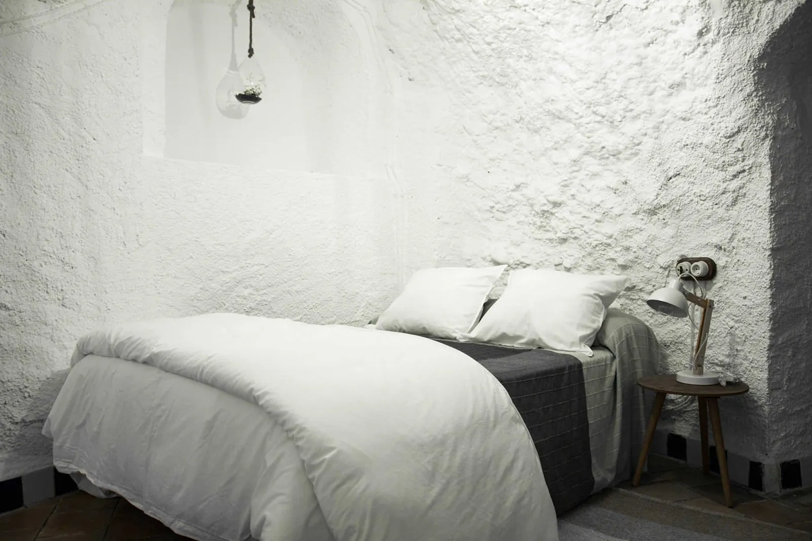 Cama individual grande con ropa blanca junto a la pared de la cueva